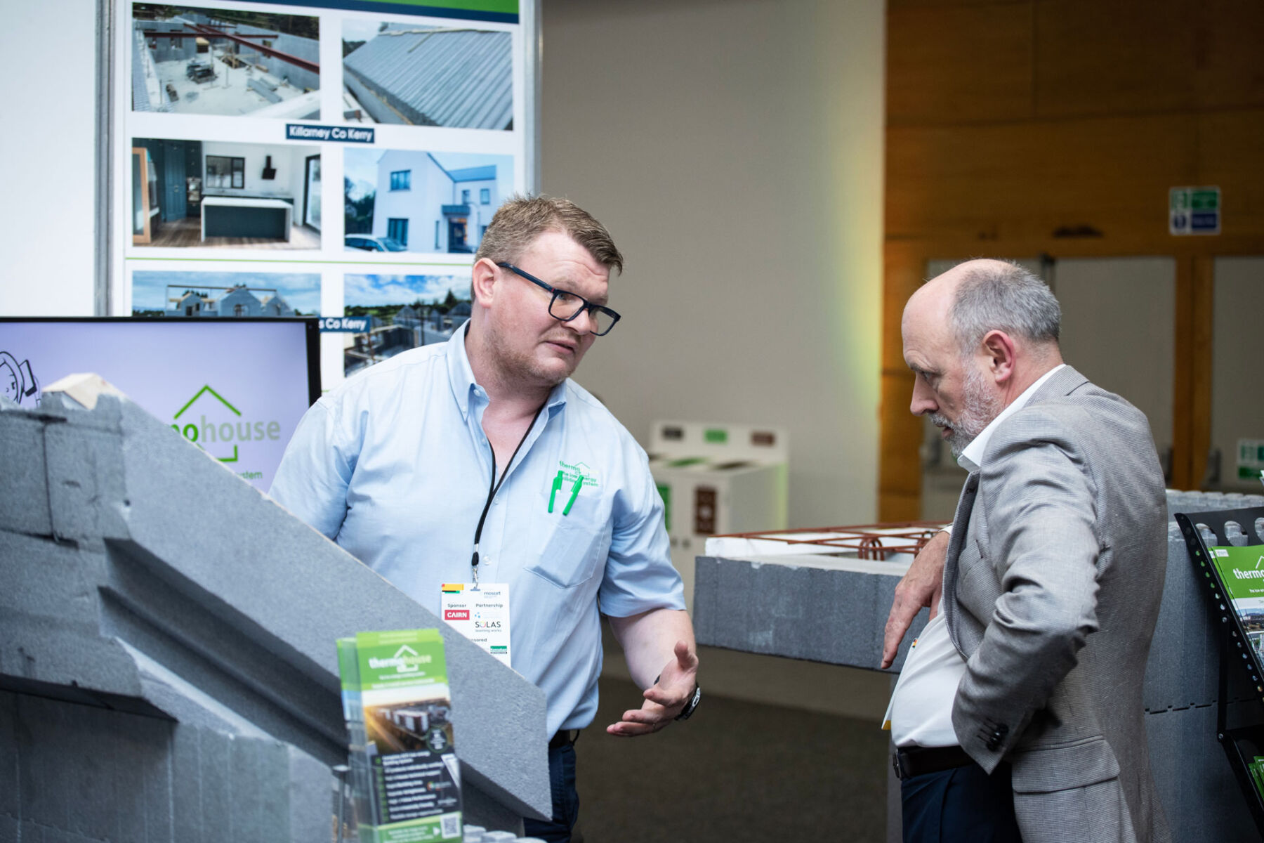 Man discusses eco-friendly building materials at a construction expo booth.