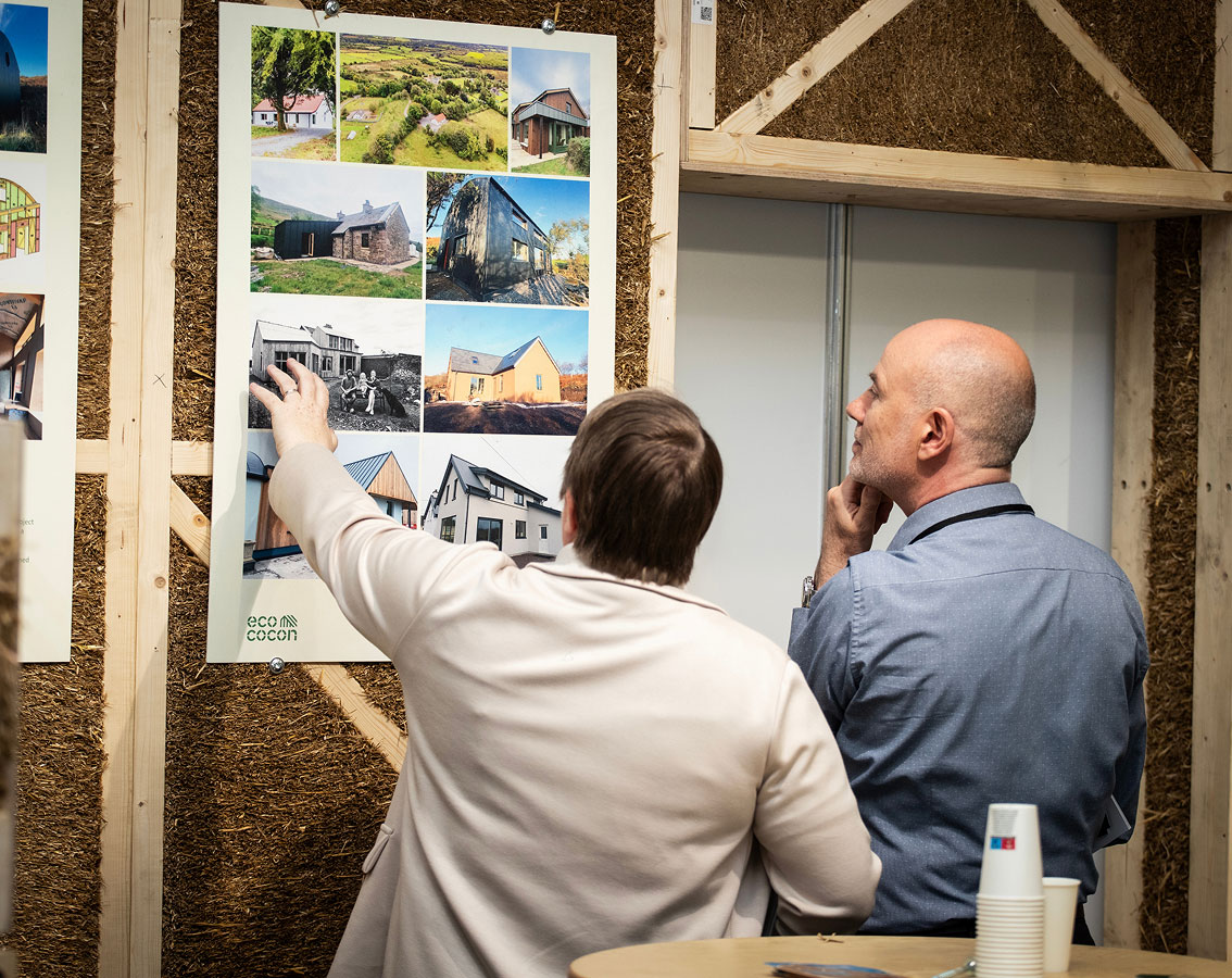 Two people discussing eco-friendly architectural designs on a display board in a workshop.