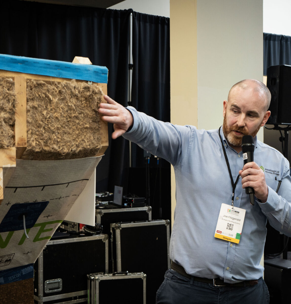 Man giving a presentation on eco-friendly insulation materials, holding a microphone and demonstrating a sample panel.